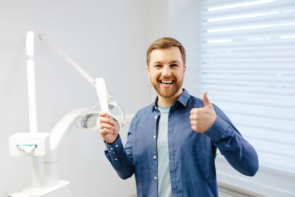 Handsome male patient looking at his beautiful smile standing at the dental office.