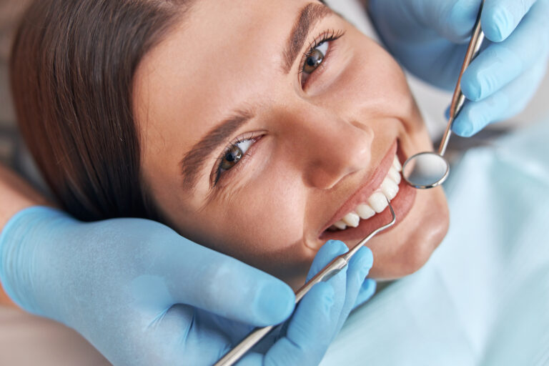 Cheerful positive dentist and client in dentistry. Female patient at dental procedure, doctor using dental instruments in modern dental clinic.