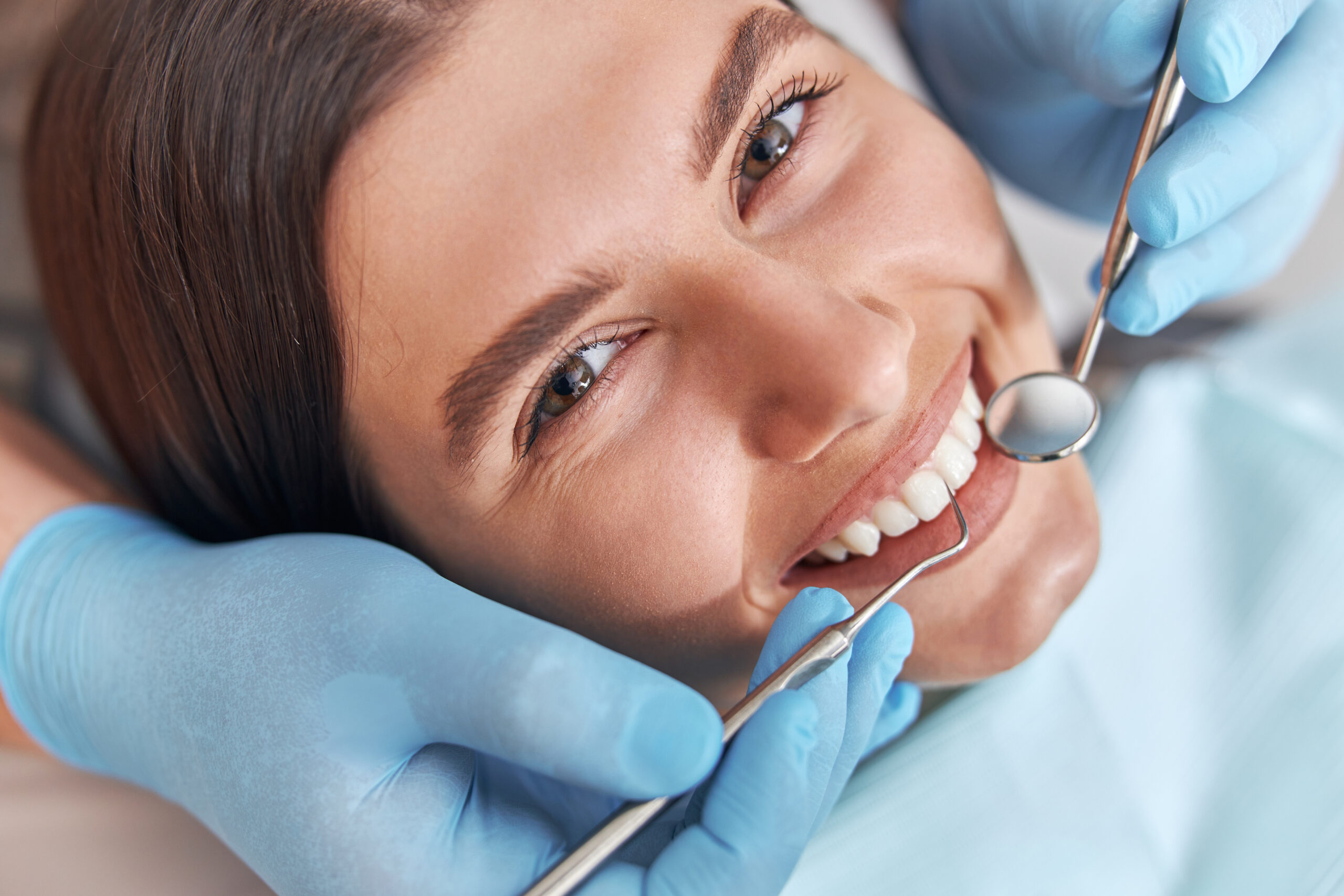 Cheerful positive dentist and client in dentistry. Female patient at dental procedure, doctor using dental instruments in modern dental clinic.
