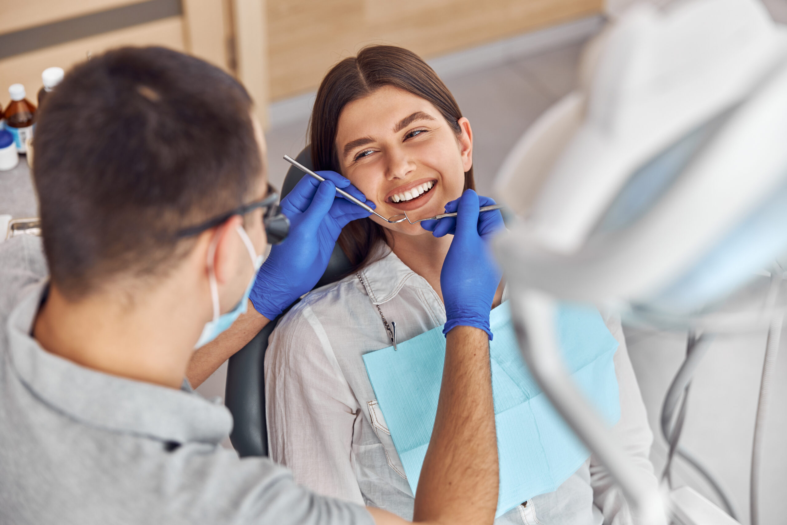 Cheerful positive dentist and client in dentistry. They look at each other and smile. Female client sit in chair.